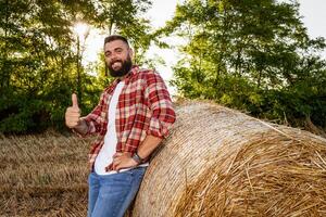 agriculteur est permanent à côté de balles de foins. il est satisfait après réussi récolte. photo