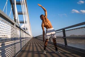 Jeune Afro-américain homme est exercice sur le pont dans le ville. il est élongation le sien corps. photo