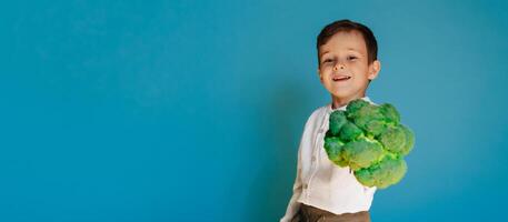 une studio coup de une souriant garçon en portant Frais brocoli sur une bleu Contexte avec une copie de le espace. le concept de en bonne santé bébé aliments. photo