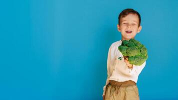 une studio coup de une garçon en portant Frais brocoli sur une bleu Contexte avec une copie de le espace. le concept de en bonne santé bébé aliments. photo