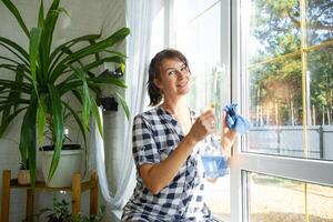 femme manuellement lavages le fenêtre de le maison avec une chiffon avec vaporisateur nettoyeur et balai à l'intérieur le intérieur avec blanc rideaux. restauration commande et propreté dans le printemps, nettoyage servir photo