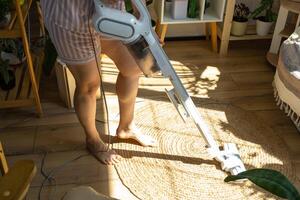 une femme aspirateurs une rond tapis dans une maison parmi maison les plantes avec une main vide nettoyeur. général nettoyage de le loger, nettoyage un service et femme au foyer photo