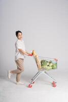 souriant femme Heureusement pousser une supermarché Chariot, isolé sur blanc Contexte photo