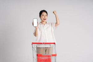 souriant femme Heureusement pousser une supermarché Chariot, isolé sur blanc Contexte photo