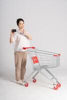 souriant femme Heureusement pousser une supermarché Chariot, isolé sur blanc Contexte photo