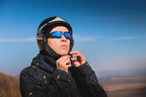 une Jeune Masculin parapente dans des lunettes de soleil attache le sien casque sur une ensoleillé journée. en train de préparer pour parapente photo