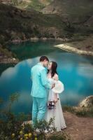 magnifique mariage couple câlins tendrement contre le toile de fond de une Montagne rivière et lac, le de la mariée longue blanc robe photo