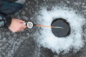 hiver pêche. fermer de une homme main en portant une pêche barre près le trou. photo