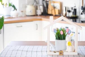 clé et minuscule maison de confortable Accueil avec Pâques décor avec lapin et des œufs sur table de cuisine. bâtiment, conception, projet, en mouvement à Nouveau loger, hypothèque, assurance, location et achat réel biens photo