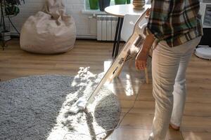 une femme aspirateurs une rond tapis dans une maison parmi maison les plantes avec une main vide nettoyeur. général nettoyage de le loger, nettoyage un service et femme au foyer photo