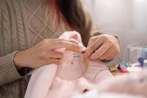 une fermer image de une femme en utilisant les ciseaux à Couper une fil sur un broderie Cadre. photo