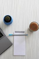 Vide carnet avec stylo sont sur Haut de bois Bureau bureau table avec une tasse de café et Bureau fournitures, Haut voir. photo