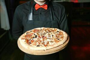 souriant homme dans tablier en portant une fraîchement cuit Pizza photo