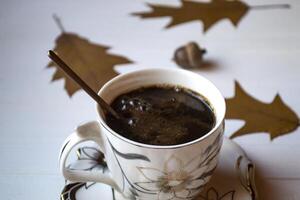 une tasse de café sur une blanc en bois tableau, et décoration par chêne l'automne feuilles. photo