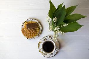 lis de le vallée, une tasse de café et dessert sur une blanc en bois tableau. photo