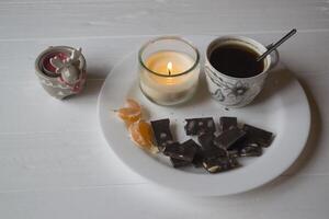 une bougie, tasse de café et noir Chocolat sur le blanc plaque. photo