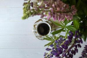 une tasse de café et lupin fleurs sur une blanc en bois tableau. photo