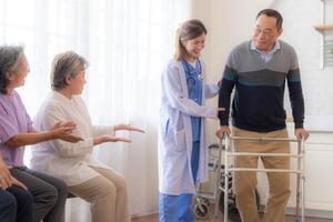 asiatique Jeune infirmière soutien Sénior plus âgée homme marcher avec marcheur. magnifique infirmière Aidez-moi et prendre se soucier. personnes âgées mature grand-père patient Faire physique thérapie avec une groupe de Sénior copains dans hôpital. photo