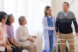 asiatique Jeune infirmière soutien Sénior plus âgée homme marcher avec marcheur. magnifique infirmière Aidez-moi et prendre se soucier. personnes âgées mature grand-père patient Faire physique thérapie avec une groupe de Sénior copains dans hôpital. photo