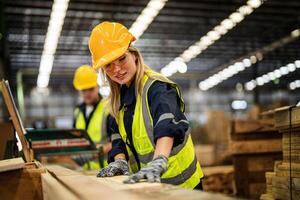 femme nettoyage Charpente bois dans foncé entrepôt industrie. équipe ouvrier Charpentier portant sécurité uniforme et difficile chapeau travail et vérification le qualité de en bois des produits à atelier fabrication. photo