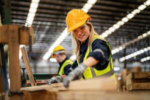 femme nettoyage Charpente bois dans foncé entrepôt industrie. équipe ouvrier Charpentier portant sécurité uniforme et difficile chapeau travail et vérification le qualité de en bois des produits à atelier fabrication. photo