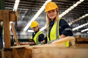 femme nettoyage Charpente bois dans foncé entrepôt industrie. équipe ouvrier Charpentier portant sécurité uniforme et difficile chapeau travail et vérification le qualité de en bois des produits à atelier fabrication. photo