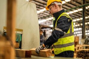 homme nettoyage Charpente bois dans foncé entrepôt industrie. équipe ouvrier Charpentier portant sécurité uniforme et difficile chapeau travail et vérification le qualité de en bois des produits à atelier fabrication. photo