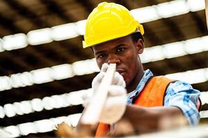 africain ouvrier Charpentier portant sécurité uniforme et difficile chapeau travail et vérification le qualité de en bois des produits à atelier fabrication. homme et femme ouvriers bois dans foncé entrepôt industrie. photo