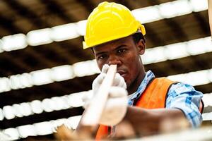 africain ouvrier Charpentier portant sécurité uniforme et difficile chapeau travail et vérification le qualité de en bois des produits à atelier fabrication. homme et femme ouvriers bois dans foncé entrepôt industrie. photo