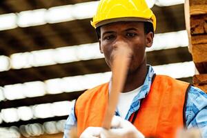 africain ouvrier Charpentier portant sécurité uniforme et difficile chapeau travail et vérification le qualité de en bois des produits à atelier fabrication. homme et femme ouvriers bois dans foncé entrepôt industrie. photo