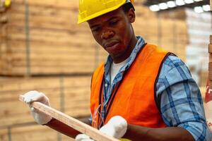 africain ouvrier Charpentier portant sécurité uniforme et difficile chapeau travail et vérification le qualité de en bois des produits à atelier fabrication. homme et femme ouvriers bois dans foncé entrepôt industrie. photo