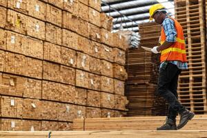 africain ouvriers homme ingénierie en marchant et inspecter avec travail suite robe et main gant dans Charpente bois entrepôt. concept de intelligent industrie ouvrier en fonctionnement. bois des usines produire bois palais. photo