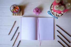 une bloc-notes avec stylo, rose cactus, froissé feuille de papier et multicolore des lettres sur une blanc en bois bureau. photo