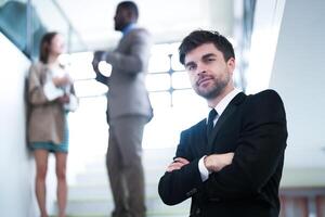 affaires gens et Bureau concept. content souriant homme d'affaire dans foncé costume. portrait de souriant milieu adulte homme d'affaire permanent à entreprise bureau. homme d'affaire souriant avec bras franchi dans bureau. photo