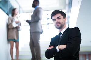 affaires gens et Bureau concept. content souriant homme d'affaire dans foncé costume. portrait de souriant milieu adulte homme d'affaire permanent à entreprise bureau. homme d'affaire souriant avec bras franchi dans bureau. photo