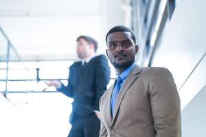 affaires gens et Bureau concept. content souriant homme d'affaire dans foncé costume. portrait de souriant milieu adulte homme d'affaire permanent à entreprise bureau. homme d'affaire souriant avec bras franchi dans bureau. photo