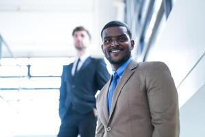 affaires gens et Bureau concept. content souriant homme d'affaire dans foncé costume. portrait de souriant milieu adulte homme d'affaire permanent à entreprise bureau. homme d'affaire souriant avec bras franchi dans bureau. photo