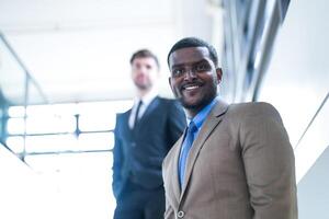 affaires gens et Bureau concept. content souriant homme d'affaire dans foncé costume. portrait de souriant milieu adulte homme d'affaire permanent à entreprise bureau. homme d'affaire souriant avec bras franchi dans bureau. photo