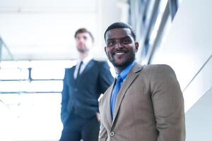 affaires gens et Bureau concept. content souriant homme d'affaire dans foncé costume. portrait de souriant milieu adulte homme d'affaire permanent à entreprise bureau. homme d'affaire souriant avec bras franchi dans bureau. photo