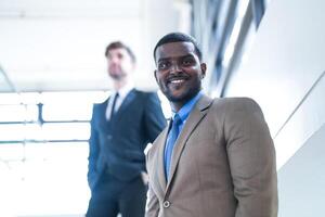 affaires gens et Bureau concept. content souriant homme d'affaire dans foncé costume. portrait de souriant milieu adulte homme d'affaire permanent à entreprise bureau. homme d'affaire souriant avec bras franchi dans bureau. photo