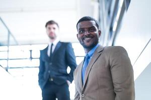 affaires gens et Bureau concept. content souriant homme d'affaire dans foncé costume. portrait de souriant milieu adulte homme d'affaire permanent à entreprise bureau. homme d'affaire souriant avec bras franchi dans bureau. photo