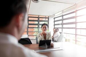 attrayant africain Jeune sur de soi femme d'affaires séance à le Bureau table avec groupe de collègues dans le Contexte. travail sur portable ordinateur. réussi femme entrepreneur. entretien Nouveau personnel. photo