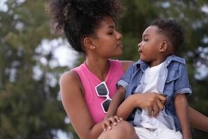 mixte course africain et asiatique mère et garçon est en jouant à le Extérieur zone. souriant content famille avoir amusement fonctionnement sur le plage. portrait de maman et enfant mode de vie avec une unique coiffure. photo