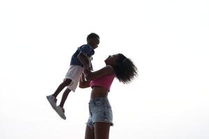 mixte course africain et asiatique mère et garçon est en jouant à le Extérieur zone. souriant content famille avoir amusement fonctionnement sur le plage. portrait de maman et enfant mode de vie avec une unique coiffure. photo