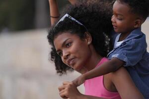 mixte course africain et asiatique mère et garçon est en jouant à le Extérieur zone. souriant content famille avoir amusement fonctionnement sur le plage. portrait de maman et enfant mode de vie avec une unique coiffure. photo