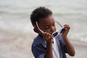 mixte course africain et asiatique garçon est en jouant à le Extérieur zone. souriant content garçon a amusement fonctionnement sur le plage. portrait de garçon mode de vie avec une unique coiffure. photo