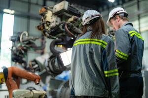 ingénieurs vérifier contrôle lourd machine robot bras. diverse équipe de industriel la robotique ingénieurs recueillies autour machine. professionnel machinerie les opérateurs réparation électrique robot sur brillant numérique panneau. photo