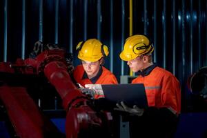 groupe de Masculin ingénieur ouvriers entretien automatique robotique bras machine dans une foncé pièce usine. ouvrier vérification et réparer automatique robot main machine. ouvrier portant sécurité des lunettes et casque. photo