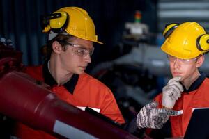 groupe de Masculin ingénieur ouvriers entretien automatique robotique bras machine dans une foncé pièce usine. ouvrier vérification et réparer automatique robot main machine. ouvrier portant sécurité des lunettes et casque. photo