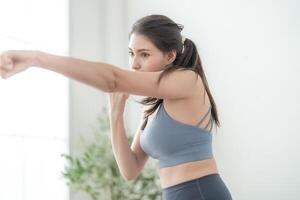 attrayant et fort femme élongation avant aptitude à intérieur maison. en bonne santé mode de vie. femme chaud en haut par boxe dans le air. Jeune femelle avec svelte corps perforation boxe jeu de jambes cardio exercer. photo